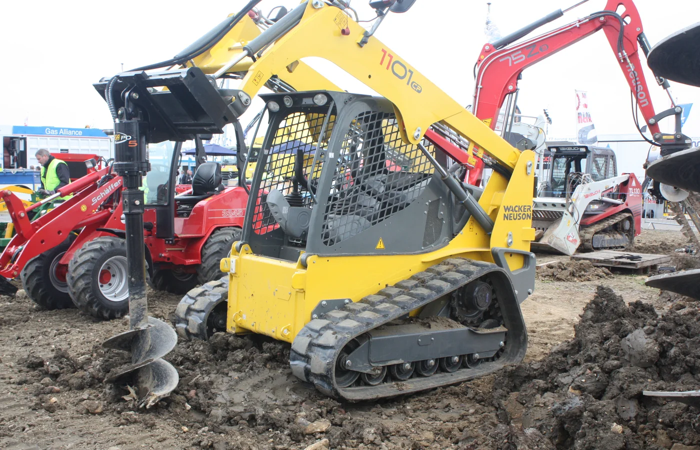 Compact tracked loader operating with a hydraulic auger attachment on disturbed ground