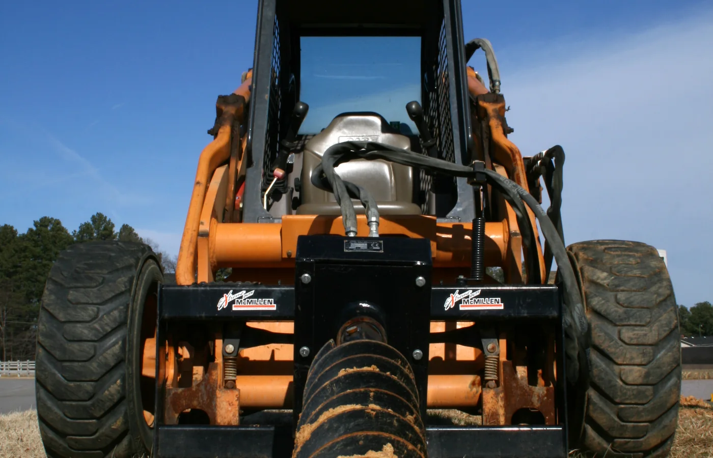 Skid steer loader viewed from the front with a hydraulic auger positioned in the soil
