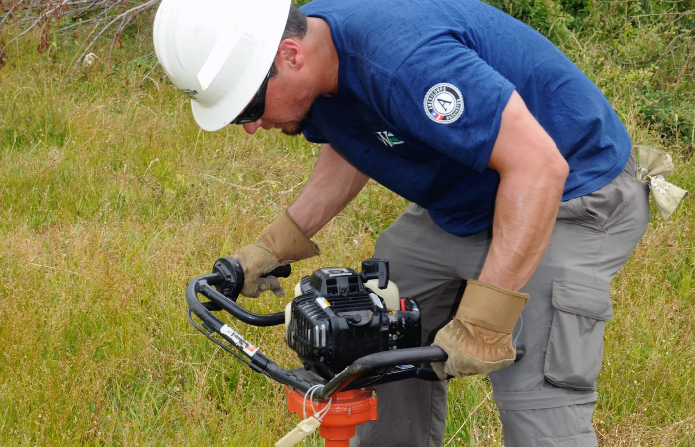 Worker drilling a post hole for replacement fencing with a powered earth auger