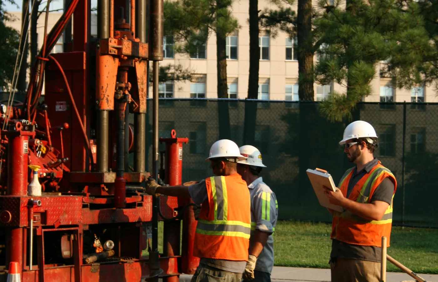 Construction crew operating vertical drilling equipment during road and foundation work