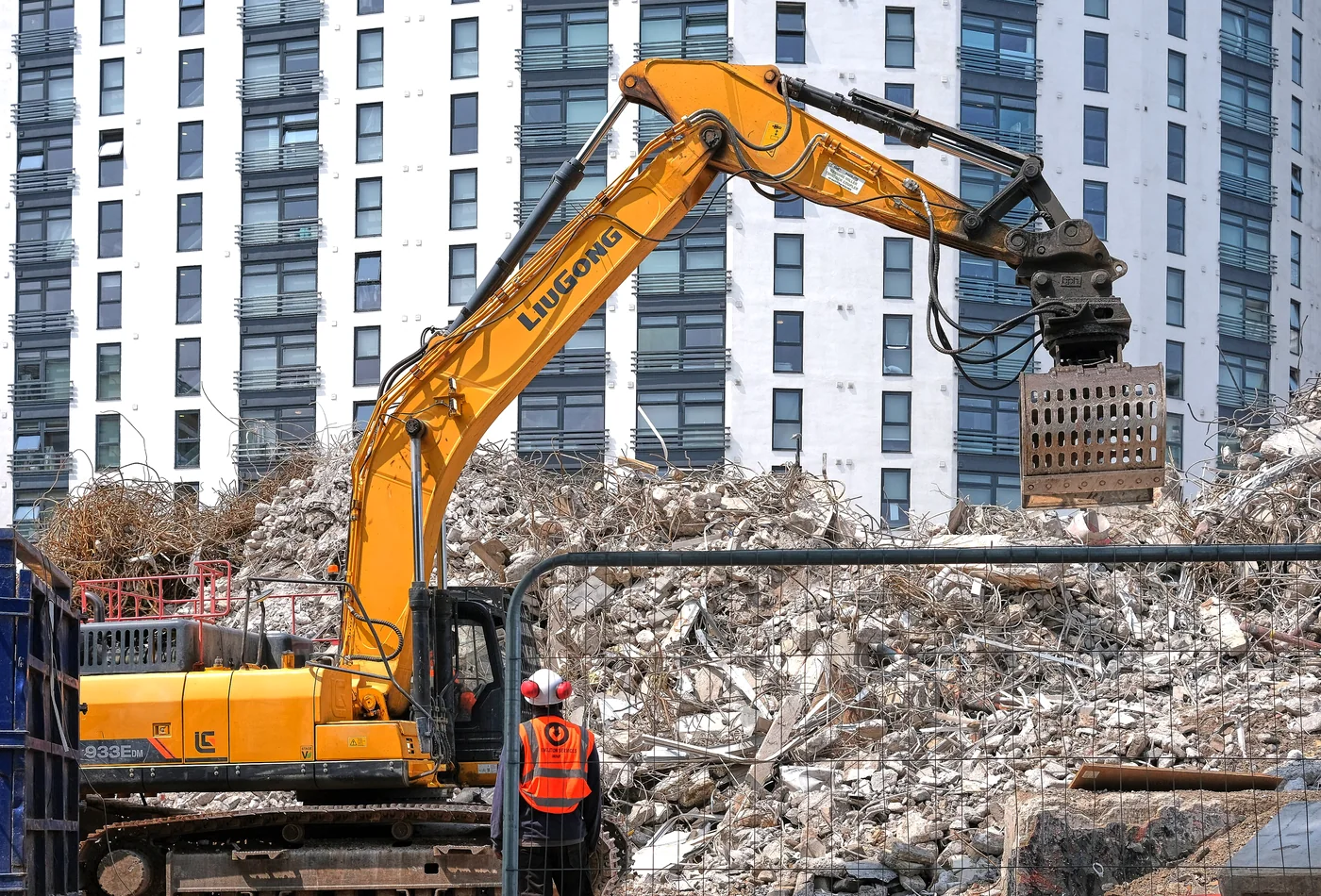 Tracked excavator with demolition grapple working on a large urban rubble pile