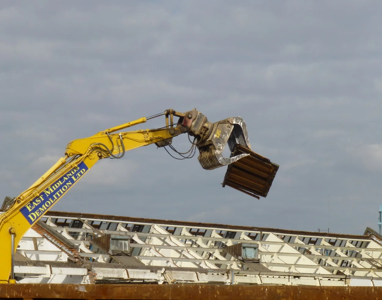 High-reach demolition excavator using a grapple to remove a roof section