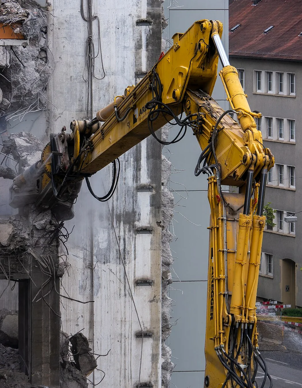 Close urban demolition work with a high-reach excavator and grapple against a concrete structure