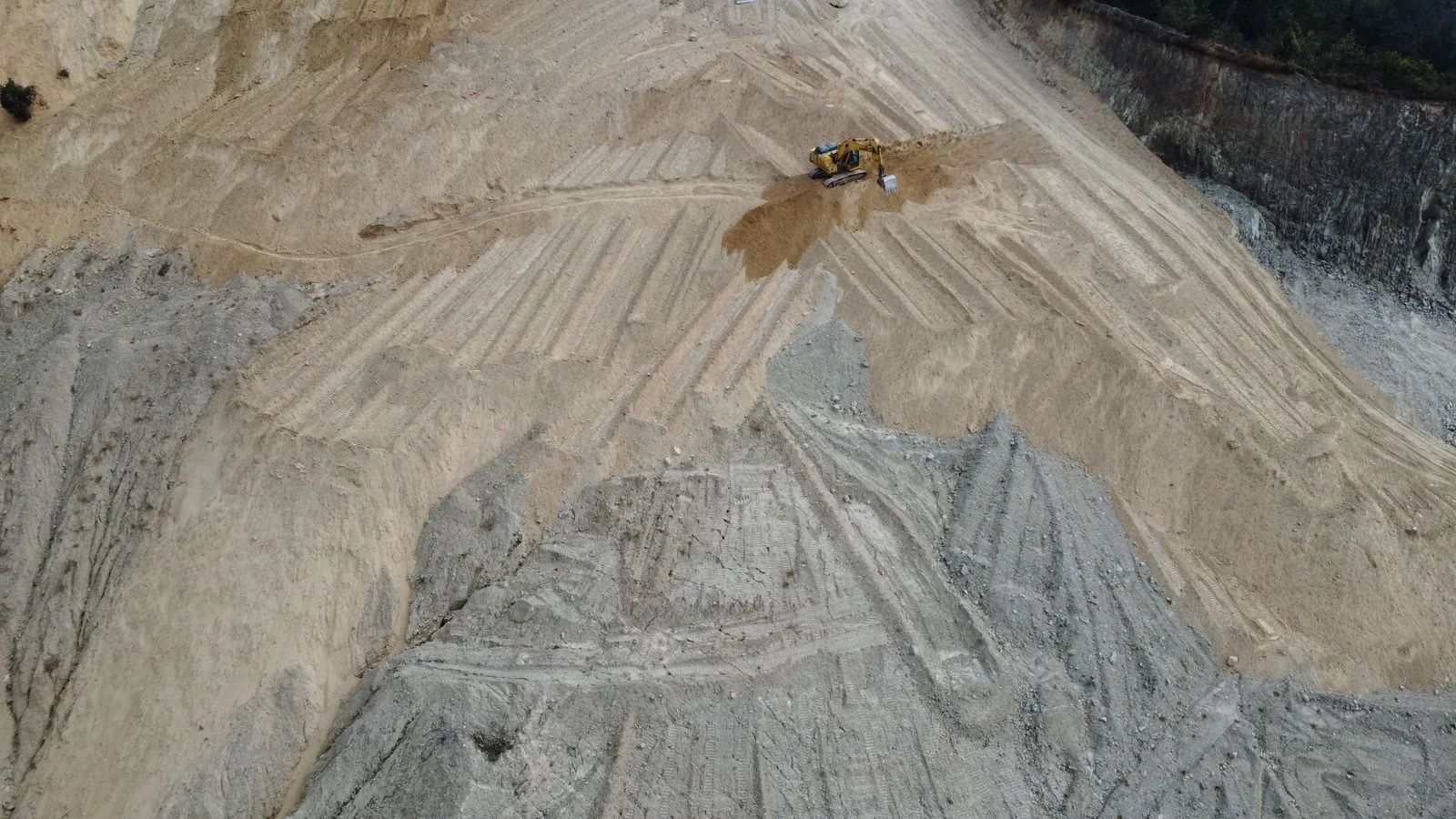 Aerial view of an excavator grading a large earthwork surface