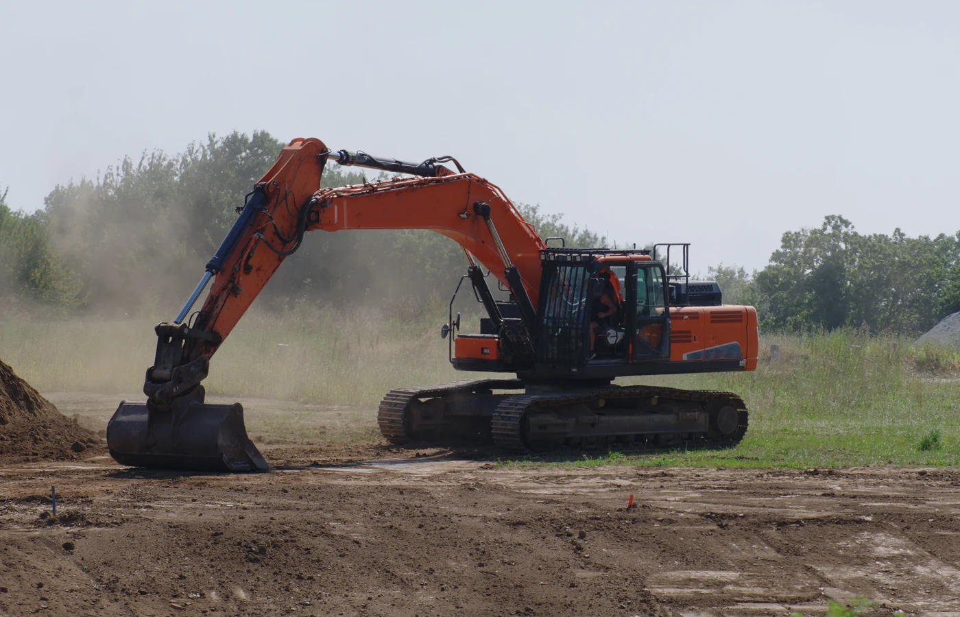 Excavator using a wide smooth-edge bucket to level soil on a construction site