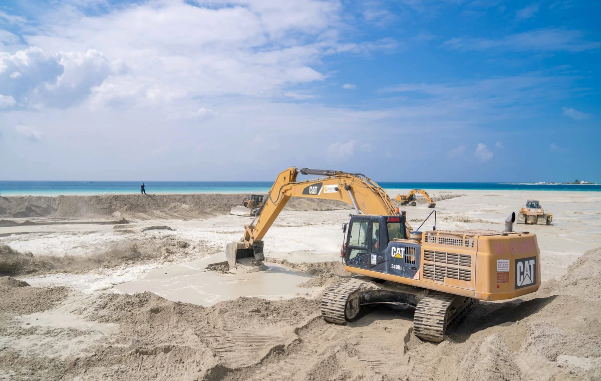 Excavator moving and grading sand on a coastal construction site