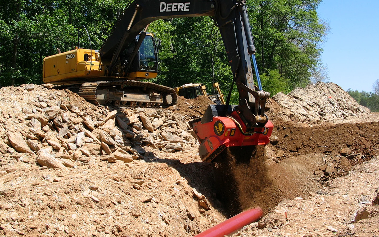 Excavator screening native material directly into a utility trench for pipeline padding