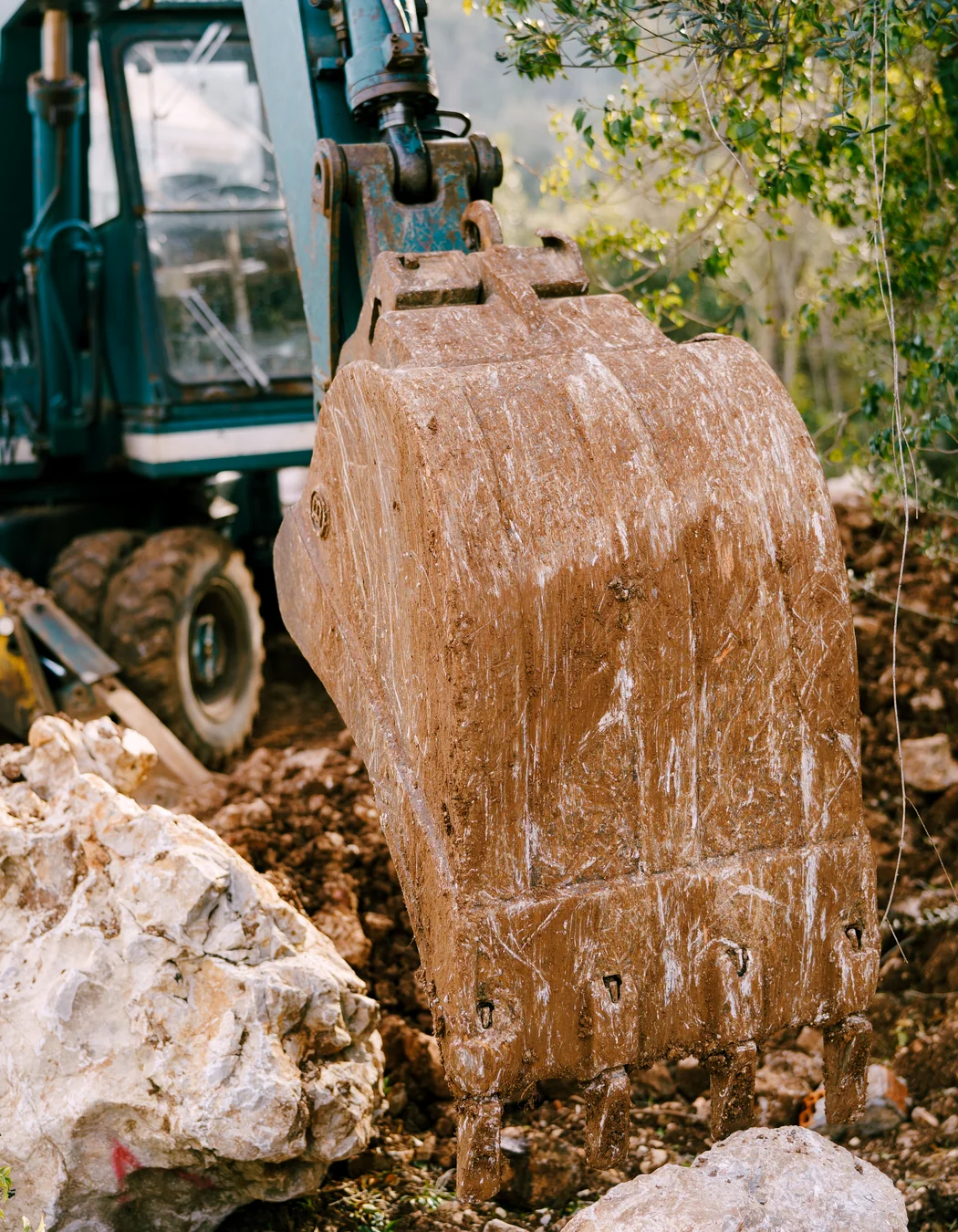 Excavator digging bucket working among large rocks, representing coarse and abrasive feed material