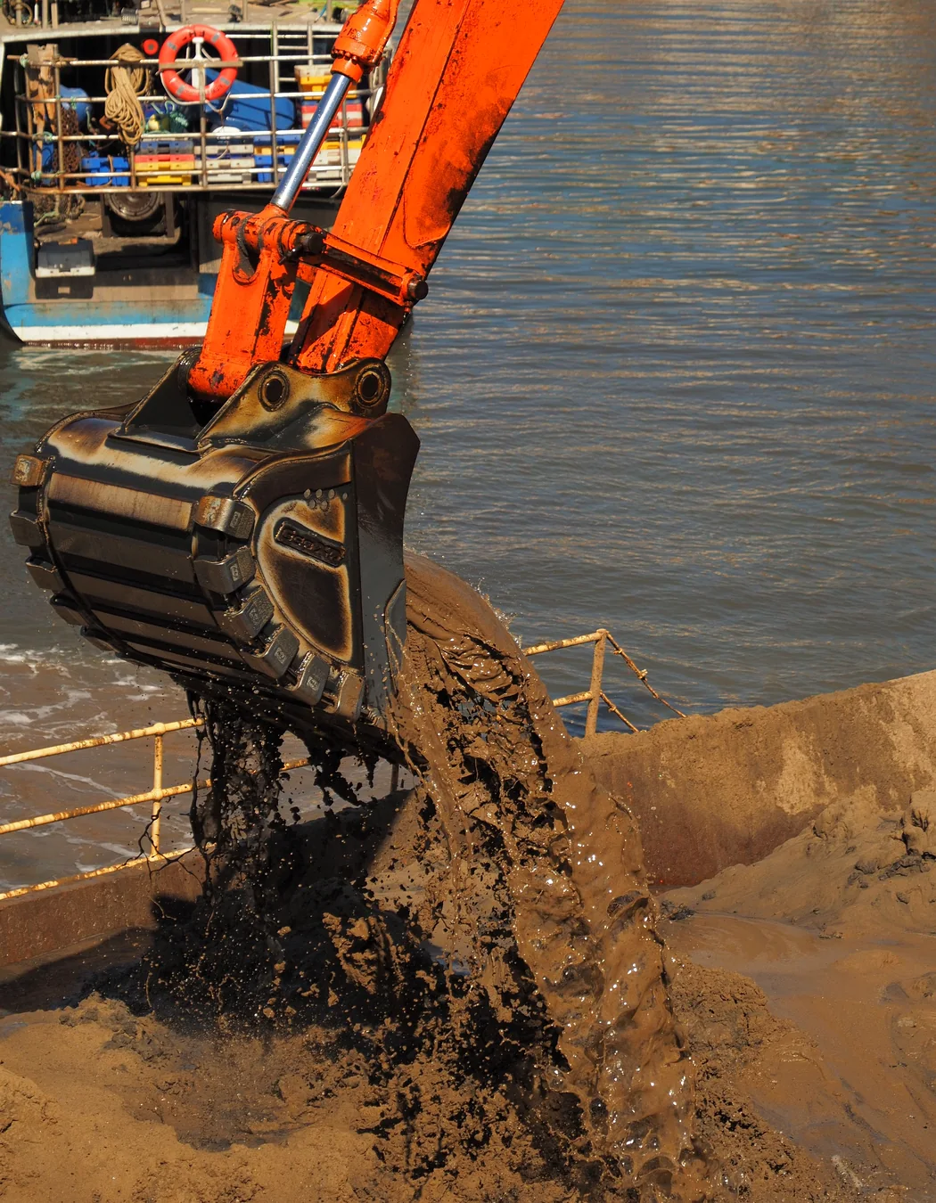 Excavator bucket discharging saturated material, illustrating wet and sticky screening conditions