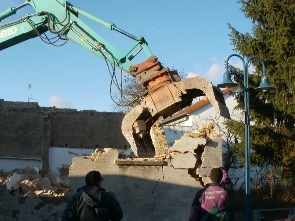 Rotating sorting grapple lifting a broken concrete section during demolition