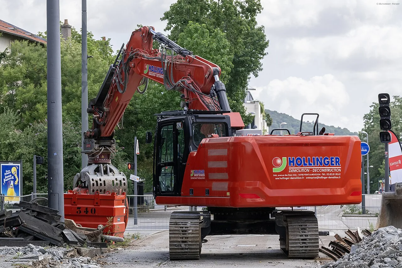 Large excavator with sorting grapple positioned over demolition containers and rubble