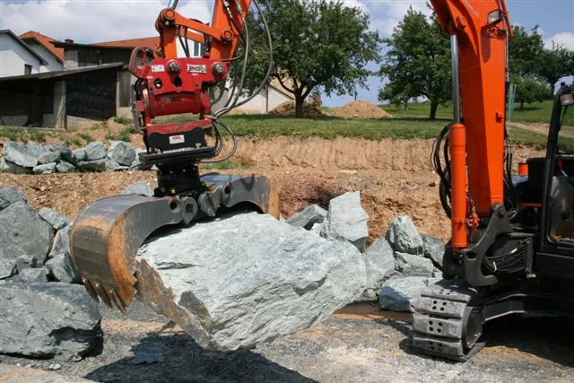 Compact excavator grapple positioning a large natural stone