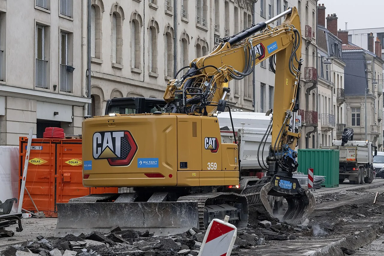 Tracked excavator with rotating grapple working on a restricted urban road site