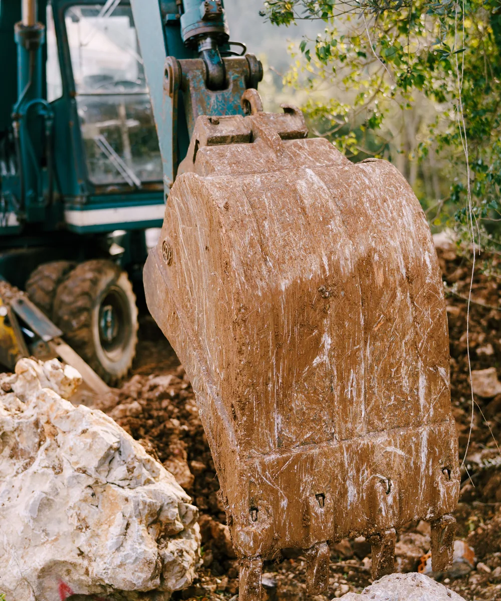 Close-up of a worn muddy excavator bucket showing shell and cutting edge