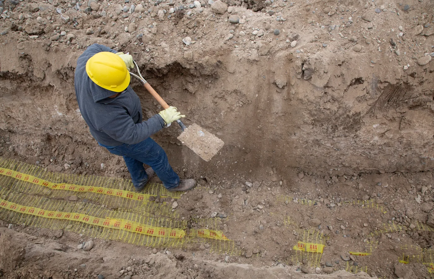 Worker inspecting a narrow excavation from inside a trench